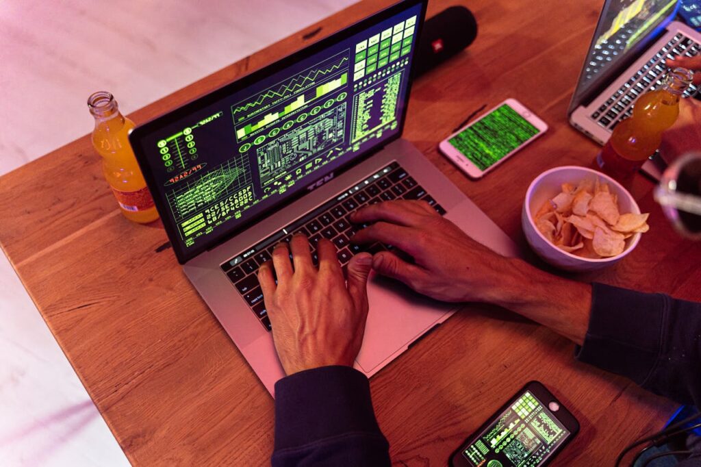 Hands typing on a laptop with coding, phone on desk, symbolizing cybersecurity.